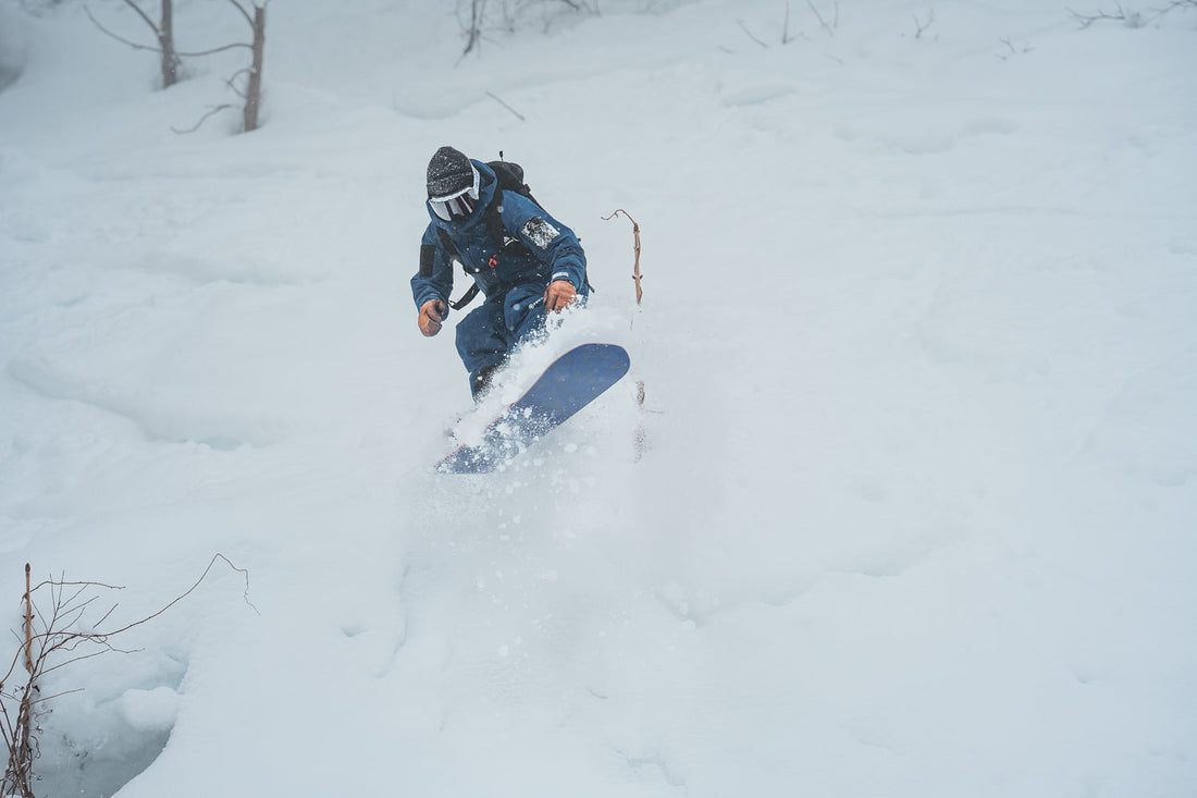Snowboarder riding deep powder through trees in Japan