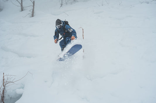 Snowboarder riding deep powder through trees in Japan
