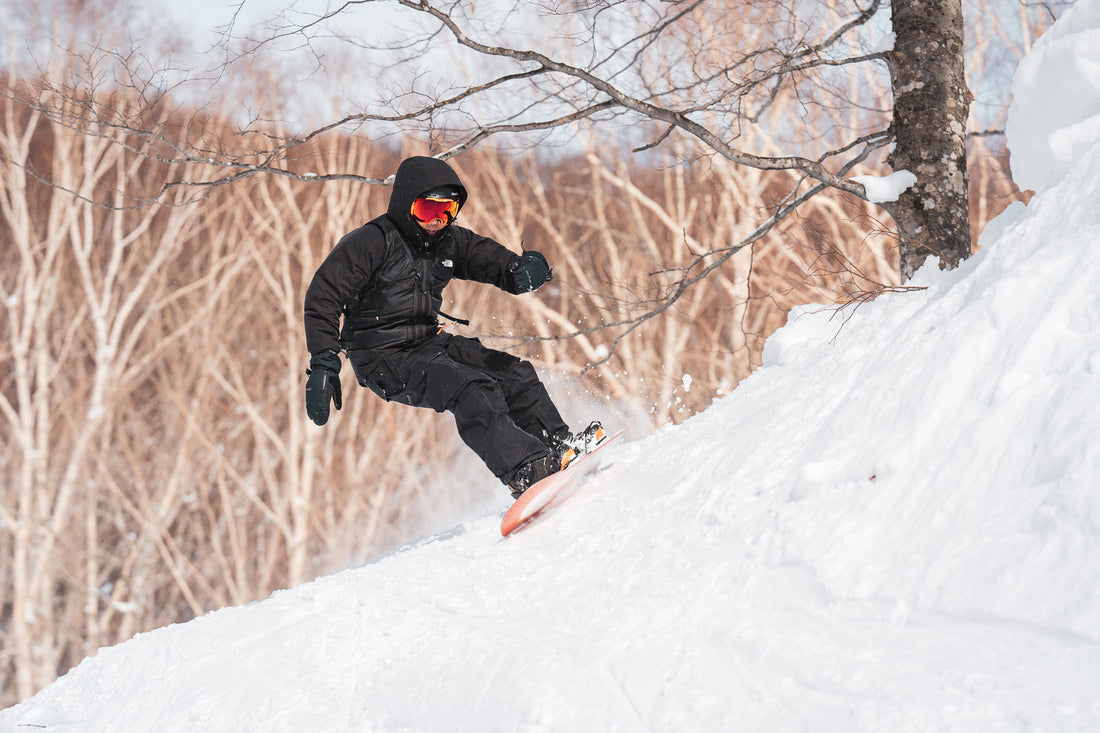 Snowboarder carving hard on packed snow through trees