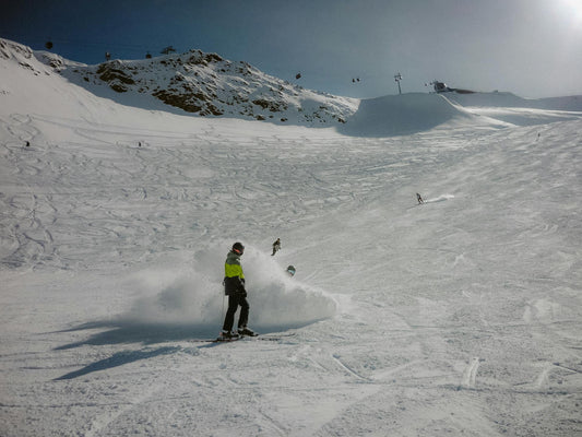 A snowboarder carving down a sunny mountain slope under clear blue sky